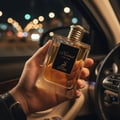 Maison Alhambra Kismet For Men by Maison Alhambra 100ml Man — Hand holding a clear glass perfume bottle with golden liquid and a gold ribbed cap, set against a blurred background of car interior and bokeh city lights at night.