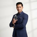 Maison Alhambra Kismet Moscow by Maison Alhambra 100ml EDP — Man in a navy blue suit holding a clear glass perfume bottle with a black label and silver cap, against a white background with shadow patterns.