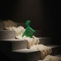 Maison Alhambra Luxe Bold – Green bottle with gold accents and 'LUXE' text, placed on textured concrete steps draped with sheer beige fabric, dark background.