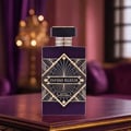Maison Alhambra Infini Elixir — A purple perfume bottle with a gold geometric design on the front, set on a dark wooden surface with a blurred opulent background.