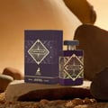 Maison Alhambra Infini Elixir — A purple perfume box and bottle with gold geometric designs and the brand's deer logo, displayed on a textured surface with rocks and sand.