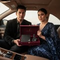 Maison Alhambra Luxe Street by Maison Alhambra – 100 ml Unisex, a couple in a car holding an open burgundy gift box containing a black perfume bottle and a black card.