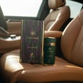Maison Alhambra Sceptre Malachite — Green perfume bottle and box with gold accents, placed on tan leather car seats.