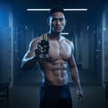Maison Alhambra Glacier Bold by Maison Alhambra 100ml EDP — Muscular man holding a dark blue perfume bottle with a gold cap and deer logo in a locker room setting