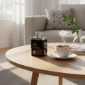 Maison Alhambra Man Black Edition — Black perfume bottle with silver cap, placed on a wooden table next to a steaming cup of coffee and a small vase with a green plant.
