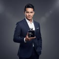 Maison Alhambra Man Black Edition — Man in a dark blue suit holding a black rectangular perfume bottle with silver cap and white text.