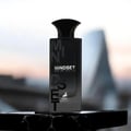 Maison Alhambra Mindset by Maison Alhambra – 100 ml For Man, a black rectangular bottle with 'MINDSET EAU DE PARFUM' text and a deer logo, set on a dark marble surface with a blurred cityscape background.