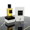 Maison Alhambra The Tux by Maison Alhambra 90ml EDP for Men — Clear glass perfume bottle with yellow liquid and black cap, displayed on a black and white stand next to its white product box on a marble surface.