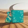 Maison Alhambra Luxe Emerald Perfume Maison Alhambra 100ml Unisex — Teal perfume bottle with gold geometric pattern and matching box, set against a desert landscape with a winding road in the background, surrounded by sparkling gold dust.