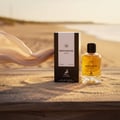 Maison Alhambra Montaigne Coco EDP — Botol dan kotak minyak wangi di atas permukaan berpasir dengan fabrik berombak di latar belakang.