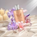 Maison Alhambra Olivia by Maison Alhambra 80ml EDP — Rose gold perfume bottle nestled among pink and purple lilies, with lit candles and decorative hairpins on satin fabric.