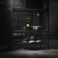 Maison Alhambra Black Origami by Maison Alhambra 100ml EDP — Botol minyak wangi hitam bertutup emas dan berlabel, diletakkan di atas rak bersebelahan tuala kelabu berlipat dan sepasang kasut sukan hitam dalam suasana bilik loker.