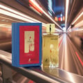 Maison Alhambra Renee Carmine EDP 100 ml Maison Alhambra — A gold perfume bottle and its blue and red box are displayed on a railing with a blurred background of moving lights.