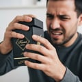 Maison Alhambra Kismet Magic by Maison Alhambra 100ml EDP Unisex — Man with disgusted expression holding a black perfume box with gold lettering, struggling to open the lid.