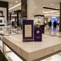 Maison Alhambra Philos Centro EDP — Purple velvet perfume bottle and matching box with gold accents, displayed on a marble surface in a retail setting.