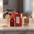 Maison Alhambra Philos Rosso 100ml EDP — Red perfume bottle with gold accents, red box, makeup brushes, lipstick, and compact on a marble vanity