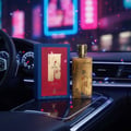 Maison Alhambra Renee Carmine EDP — Gold perfume bottle and blue box with red accents on a car's center console, with blurred city lights in the background.