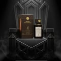 Maison Alhambra Smoked Oud & Vanilla by Maison Alhambra 100ml EDP — A brown box and a dark glass perfume bottle with a gold cap, both featuring the brand's logo and product name, are displayed on a dark, ornate throne-like structure with smoky wisps in the background.