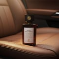 Maison Alhambra Smoked Oud & Vanilla by Maison Alhambra 100ml EDP — Amber glass perfume bottle with a dark cap and gold emblem, placed on brown leather car seats.
