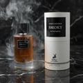 Maison Alhambra Smoky by Maison Alhambra 100ml EDP Unisex — A glass perfume bottle with amber liquid and a black cap sits next to its cylindrical packaging, surrounded by wisps of smoke against a dark marble background.