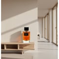 Maison Alhambra Smoky by Maison Alhambra 100ml EDP Unisex — A clear glass perfume bottle with amber liquid and a black cap, labeled 'SMOKY', sits on a light wood shelf against a textured wall with shadows.