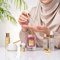 Maison Alhambra So Candid by Maison Alhambra 100 ml EDP — Woman applying serum from a dropper bottle onto her palm, with the So Candid perfume bottle and other skincare products on a white surface.