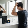 Maison Alhambra Spectrum by Maison Alhambra 100ml EDP Men — Man styling hair in front of a bathroom mirror, with the perfume bottle and box on the counter.