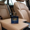 Maison Alhambra Spectrum by Maison Alhambra 100ml EDP Men — Blue glass perfume bottle with gold cap and label, placed on a tan leather car armrest with car seats in the background.