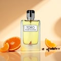 Maison Alhambra Toro Pour Homme – A clear glass bottle of yellow perfume with a silver and black cap, placed on a reflective surface with orange slices and peppercorns.