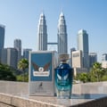 Maison Alhambra Victorioso Legend oleh Maison Alhambra 100 ml untuk Lelaki — Botol minyak wangi kaca biru dan kotaknya berdiri di atas permukaan batu dengan Menara Berkembar Petronas di latar belakang.