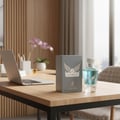 Maison Alhambra Victorioso by Maison Alhambra 100ml EDP Men — A grey box and a clear glass perfume bottle with blue liquid sit on a wooden desk next to a laptop and a potted orchid.