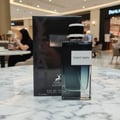 Maison Alhambra Yeah by Maison Alhambra 100ml EDP Men — Black box and glass bottle of fragrance with white label 'YEAH! MAN' on a marble surface, blurred background of a shopping mall.