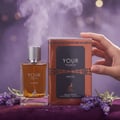 Maison Alhambra Your Touch Intense — A glass perfume bottle with amber liquid and a silver ribbed cap, next to its copper and black box, with lavender sprigs and smoke effects.