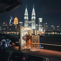 Nafahat Oud Maluky by Nafahat 100ml Unisex — Kotak dan botol minyak wangi beraksen emas dipamerkan di papan pemuka kereta pada waktu malam, dengan latar belakang Menara Berkembar Petronas dan langit bandar.