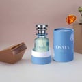 Osma Osma Ambry A Fresh & Fly 75ml EDP — A light green perfume bottle with a silver cap, presented in a light blue cylindrical box, with a piece of amber and a chocolate bar prop.