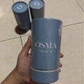 Osma Osma Floral A Ginger Blossom 75ml — A hand holds a light blue cylindrical perfume box with 'OSMA FLORAL A' printed in white. Two similar boxes are blurred in the background.
