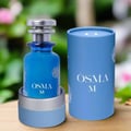 Osma Osma M Pineapple & Vanilla 150ml EDP — Blue perfume bottle with silver cap, displayed in a blue and silver holder, next to its cylindrical blue packaging box with white floral accents.