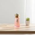 Paris Corner Khair Fusion — Botol minyak wangi kaca beku merah jambu dengan penutup berhias emas dan hijau, diletakkan di atas meja kayu bersama buku dan pokok sukulen mini.