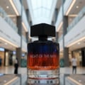 Paris Corner Night of the Man by Pendora Scents Paris 100ml — Botol minyak wangi kaca bertutup hitam, cecairnya berwarna biru ke jingga, diletakkan di hadapan latar belakang pusat beli-belah yang kabur.