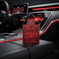 Rayhaan Rayhaan Crimson for Men 100ml — A red, intricately patterned perfume bottle with a geometric design sits on a black leather car console, with a blurred car dashboard and red ambient lighting in the background.