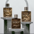 Rayhaan Imperia Collection 100ml for Man — Tiga botol minyak wangi kaca berlabel corak emas dan hitam, dipamerkan di atas alas batu bertingkat dengan tumbuhan menjalar.