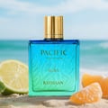 Rayhaan Pacific Elegant EDP 100 ml Men — Botol minyak wangi kaca gradien biru dan hijau dengan penutup emas, diletakkan di atas pasir bersama hirisan limau dan potongan oren di hadapan, dengan latar belakang pantai dan laut yang kabur.