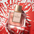 Rue Broca Pride Pour Femme EDP — A square glass perfume bottle with pink liquid and a gold cap, placed on a white and red abstract splatter background.