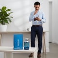 Volare Reload Blue by Volare Man – 100 ml for Him perfume bottle and box displayed on a white table, with a man in the background holding a wallet and keys.