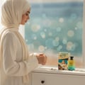 Volare Santorini Beaches — Woman in hijab looking at perfume box and bottle on dresser with blurred beach background