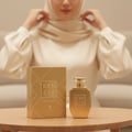 Volare Vanilla Irish by Volare – 100 ml for Women. A gold perfume bottle and its matching box are placed on a wooden table, with a woman adjusting her hijab in the blurred background.