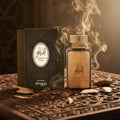 Zimaya Al Embratur Elixir by Zimaya 100ml EDP — A gold-embossed perfume bottle and its dark green box sit on a carved wooden surface with scattered oud chips and smoke rising.