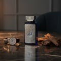 Zimaya Al Embratur Intense by Zimaya 100ml EDP Men — Blue glass perfume bottle with ornate silver label and cap, next to a classic wristwatch and oud wood pieces on a marble surface.