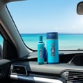 Zimaya Andalusi Blue by Zimaya 100ml EDP Men — Teal perfume bottle and cylindrical box with blue and white mosaic pattern, placed on a car dashboard with a bright blue ocean and sky in the background.
