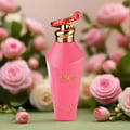 Zimaya Hawwa Pink by Zimaya Women 100ml EDP — Pink perfume bottle with gold spiral cap adorned with a red and gold patterned accent, set against a soft focus background of pink and white roses.